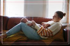 A woman with bowel problems after pregnancy sits on a brown couch with her newborn resting on her legs
