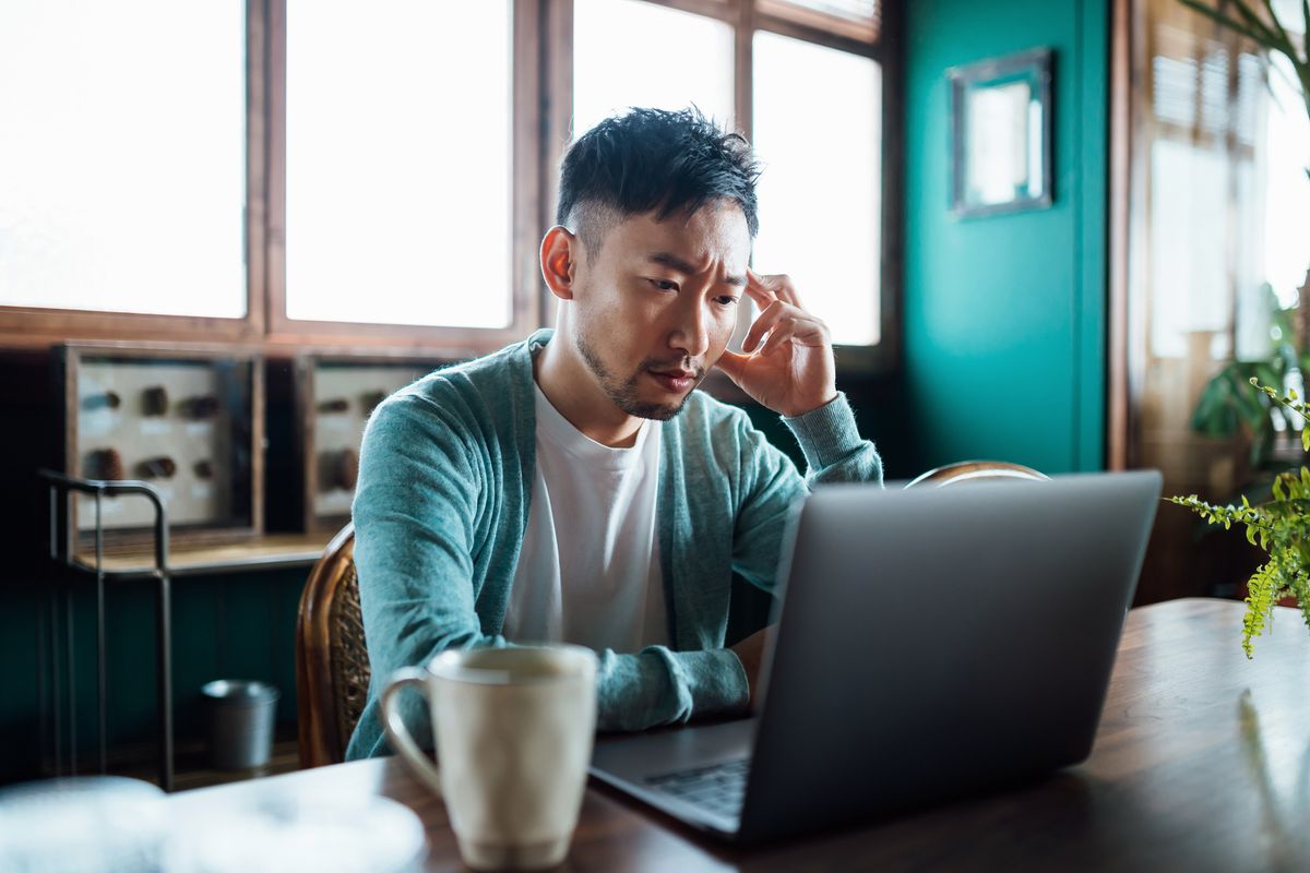 A man sat in front of a laptop at home with a concerned look on his face