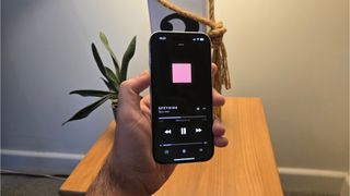 Apple iPhone 16 smartphone held in hand in front of wooden table with music app on screen