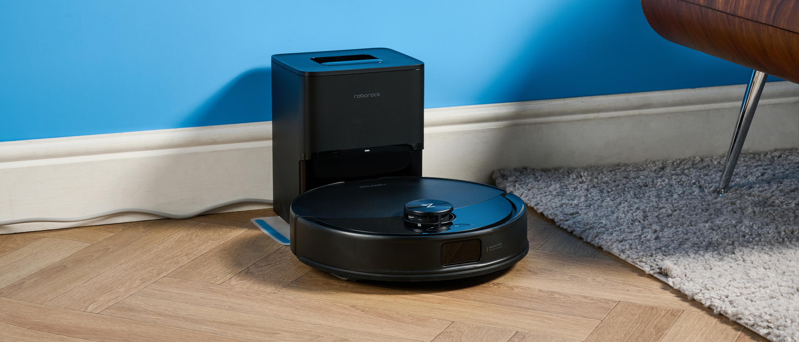 Roborock Q10 S5+ photographed on a wooden floor in front of a blue background