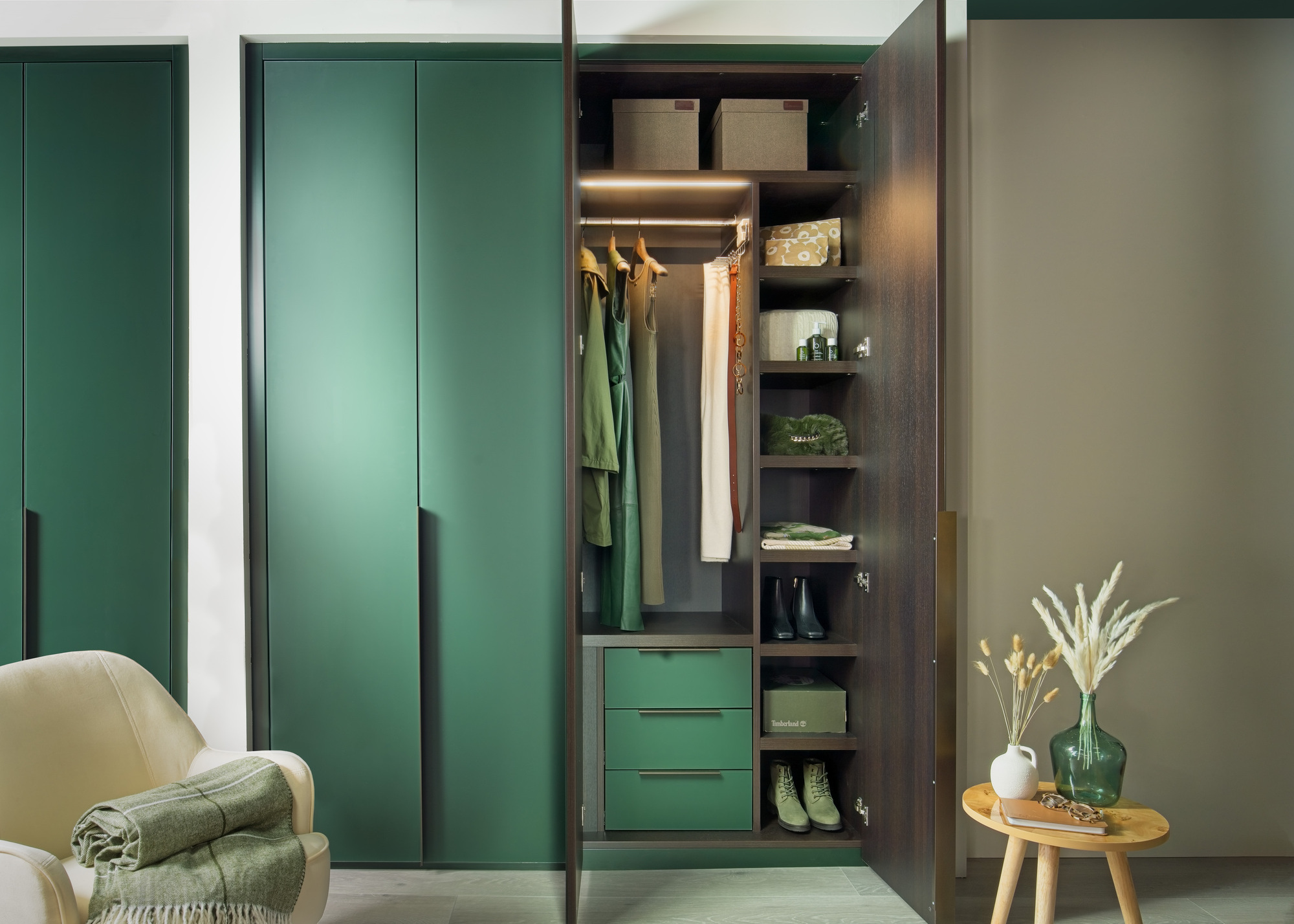 A green closet with the door open displaying clothes on a rod and shelving with storage boxes on the top shelf