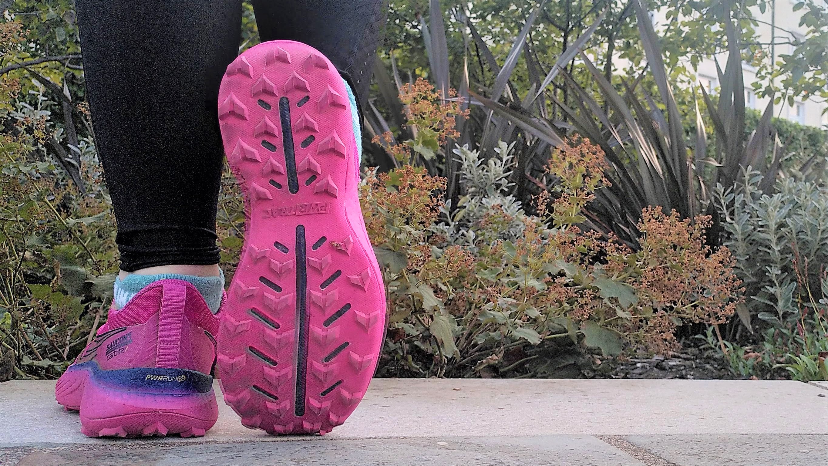 A runner's feet wearing bright pink Saucony Endorphin Edge shoes showing the sole of one of the shoes