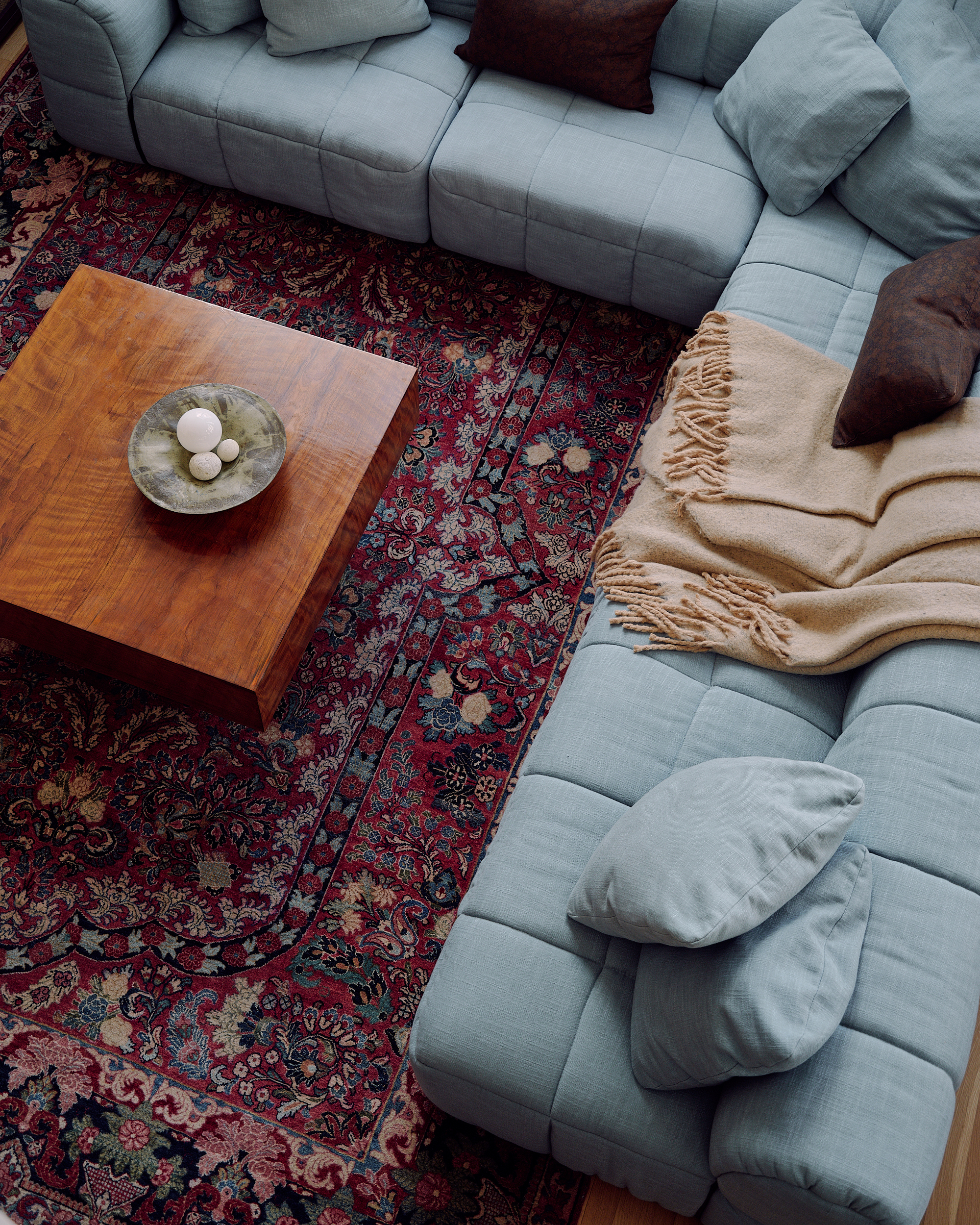 Image from above of a large, light blue sectional sofa on a red patterned rug. There is a wooden coffee table on the rug.