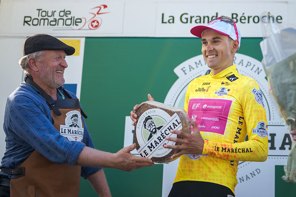 France's Alex Baudin (EF), wearing the overall leader's yellow jersey, receives a cheese as he celebrates during the podium ceremony of the second stage of the Tour of Romandie UCI cycling World tour, 157km loop from the start to the finish in La Grande Beroche, in Saint-Aubin-Sauges on May 1, 2025. (Photo by Fabrice COFFRINI / AFP)