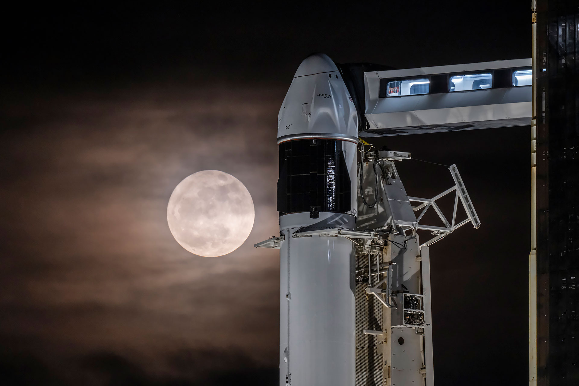 Una luna llena brilla a través de un cielo parcialmente nublado para encender un cohete y su cápsula espacial en la plataforma de lanzamiento