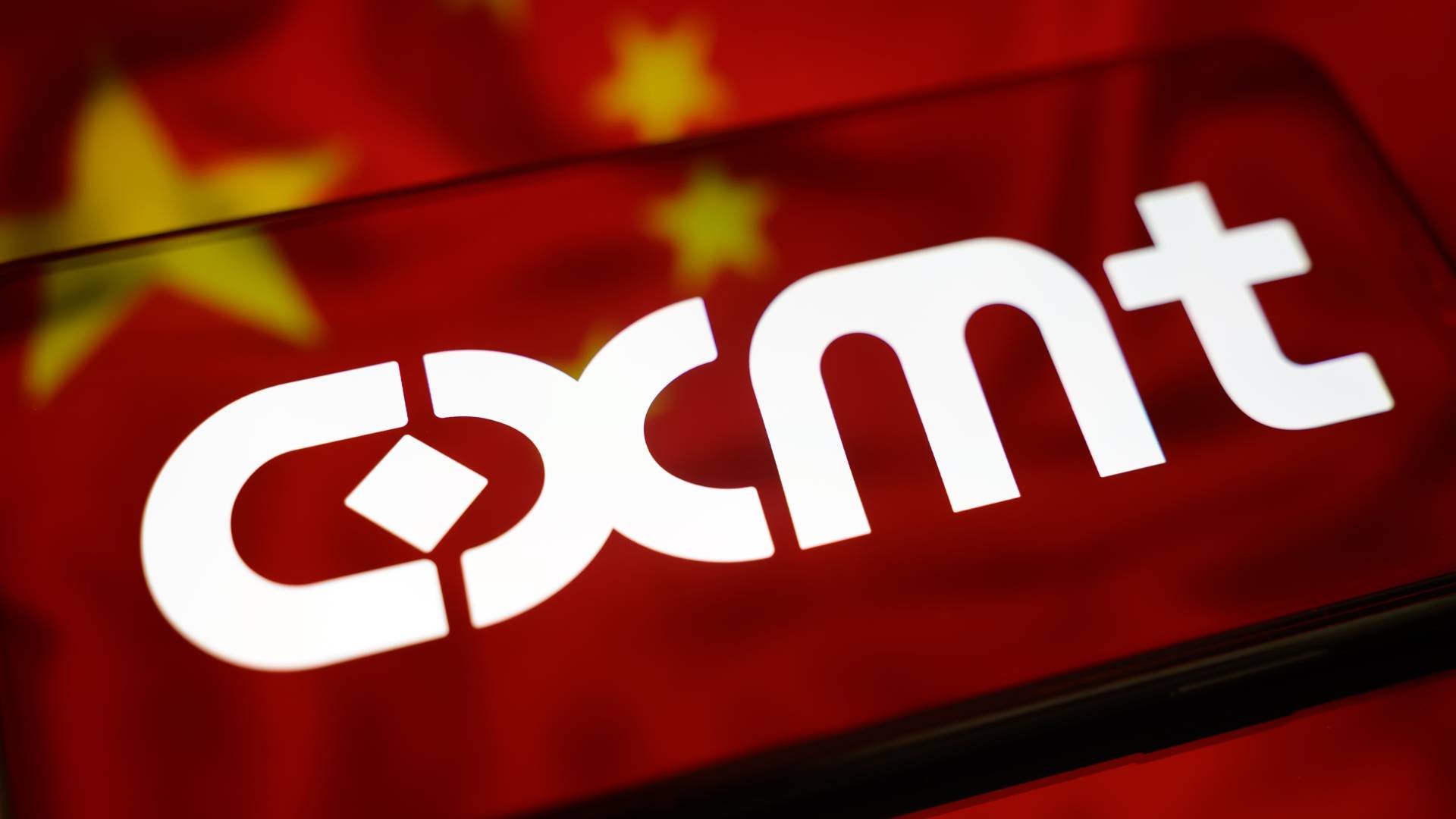 The CXMT logo is displayed on a smartphone screen placed on a reflective surface on which the flag of China is projected.