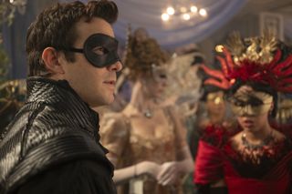 A man in a black mask (Luke Thompson as Benedict Bridgerton) stands in front of women in Regency costumes and masks, in 'Bridgerton' season 4.