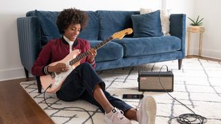 Woman sits on the floor playing her pink Fender Strat through a Spark amp