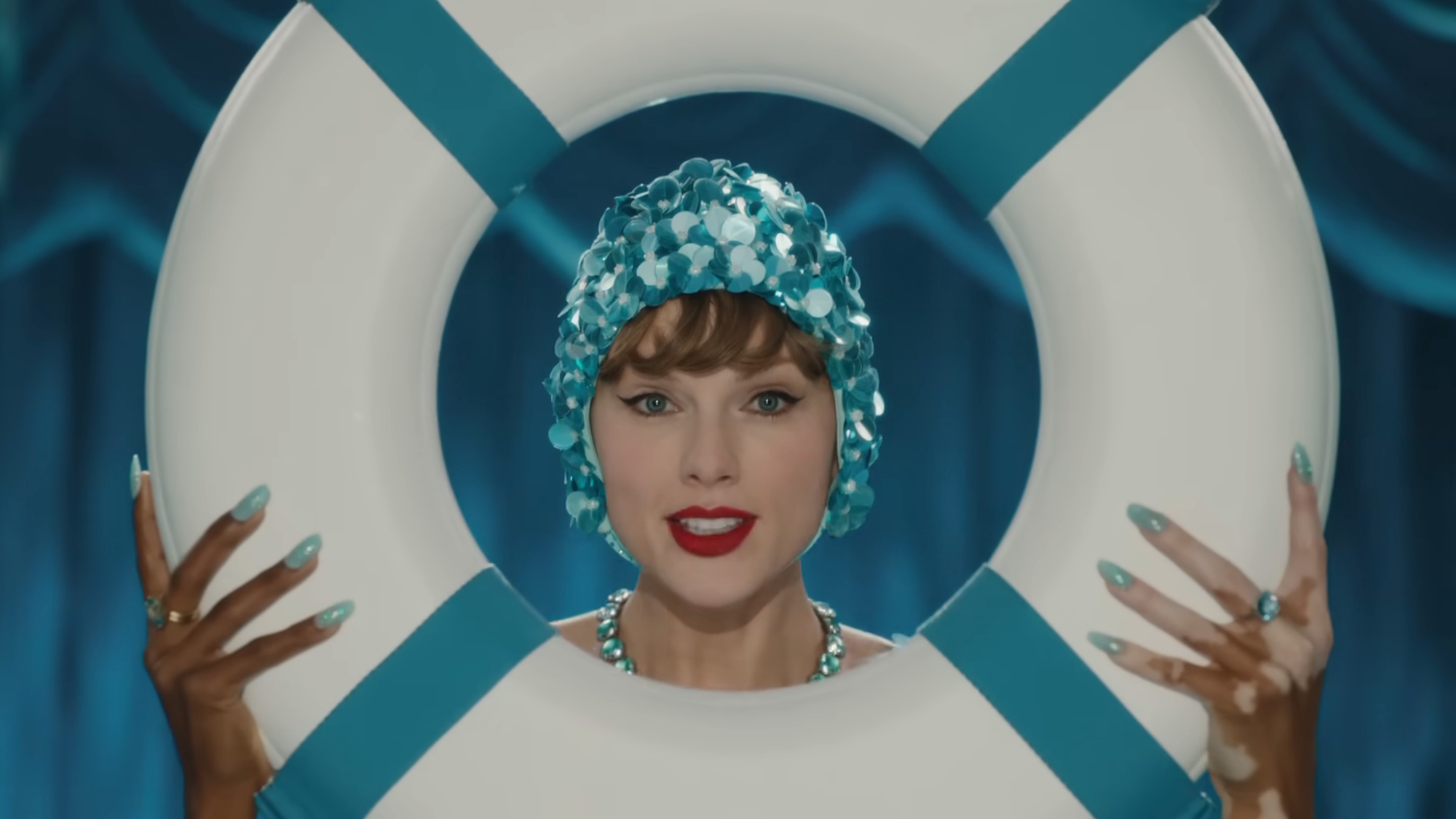 Taylor Swift is shown in the music video for The Fat of Ophelia, wearing a sparkly blue swim cap as her face peeks through the middle of a white life preserver.