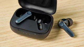 A photo of the EarFun Air Pro 4 earbuds with one inside and one outside of the case, on a wooden surface