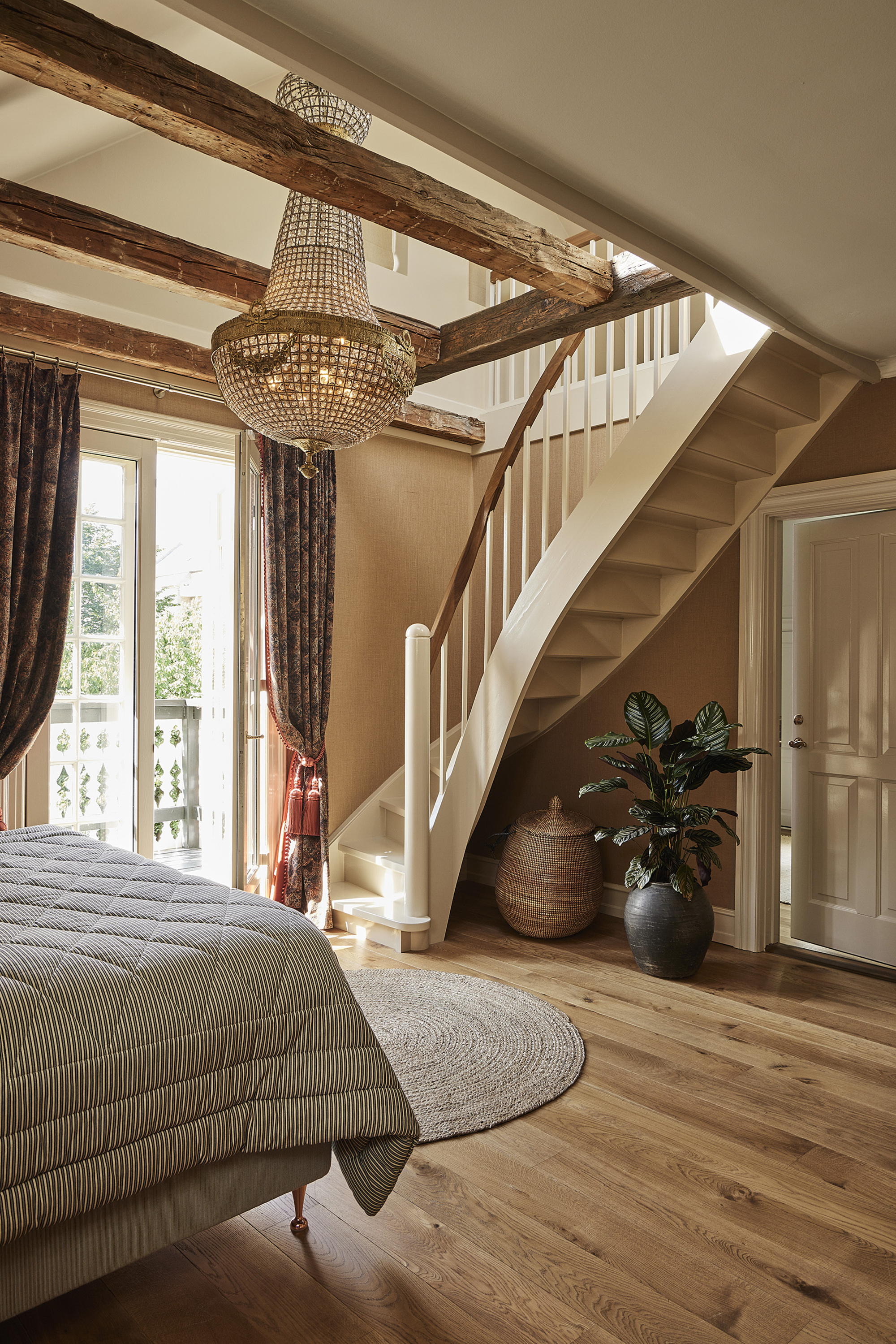 A bedroom with wooden flooring, a striped comforter on the bed, and a staircase leading into a loft