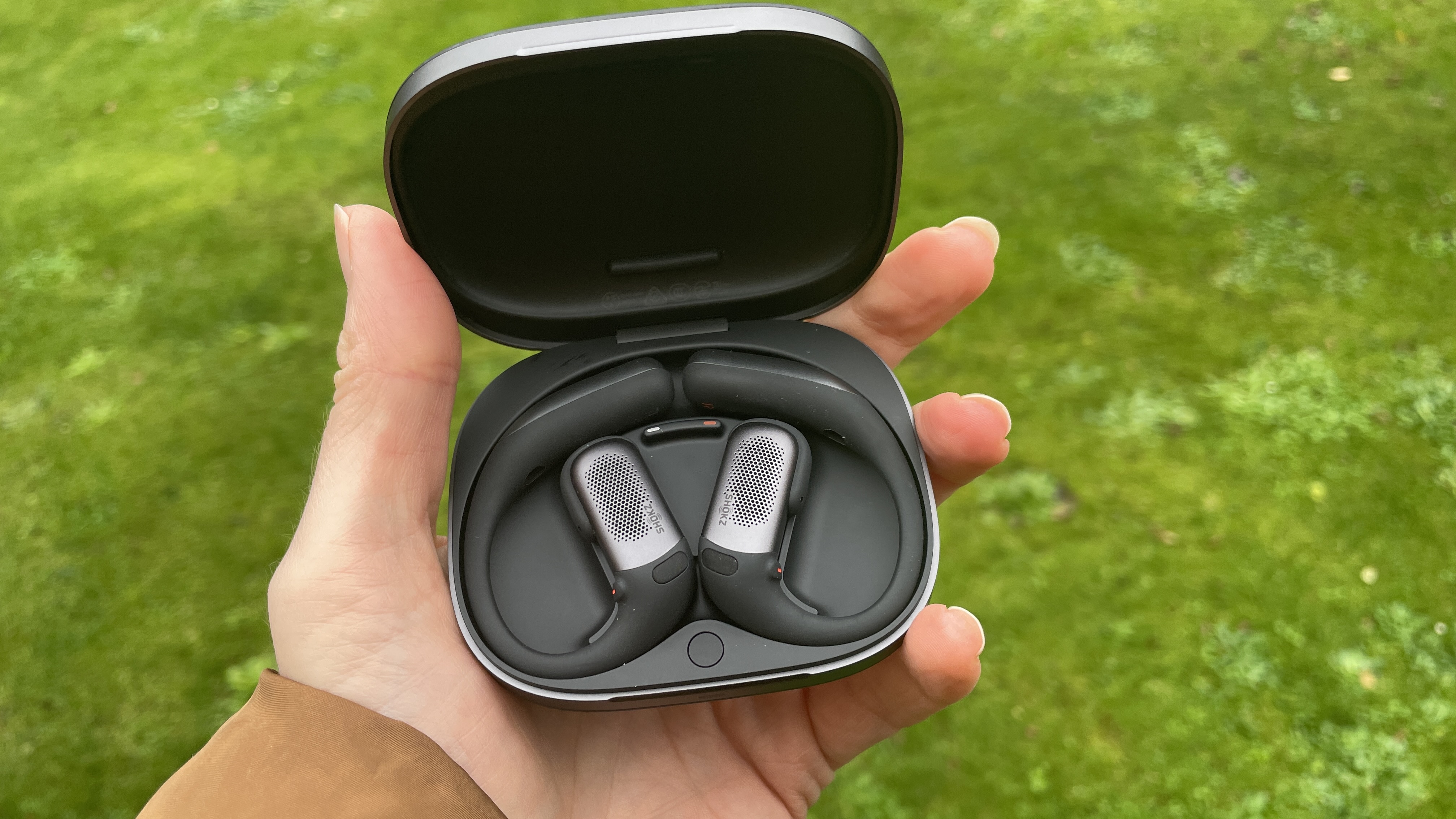 Shokz Openfit Pro outside, outside held in a woman's hand, with green grass in the background