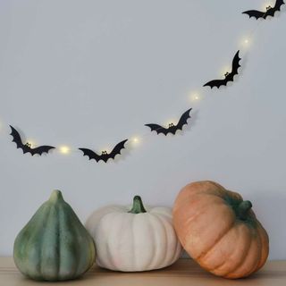 Bat halloween gardland with LED light up eyes on wall with pumpkins below 