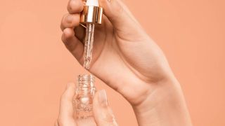 A bottle of serum in someone's hands on an orange background