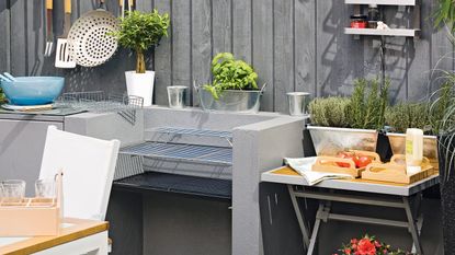 Corner of garden with tabletop BBQ, festoon lighting and potted plants