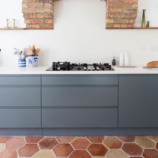 Hexagon shaped terracotta floor tiles with blue kitchen cabinets and white wall