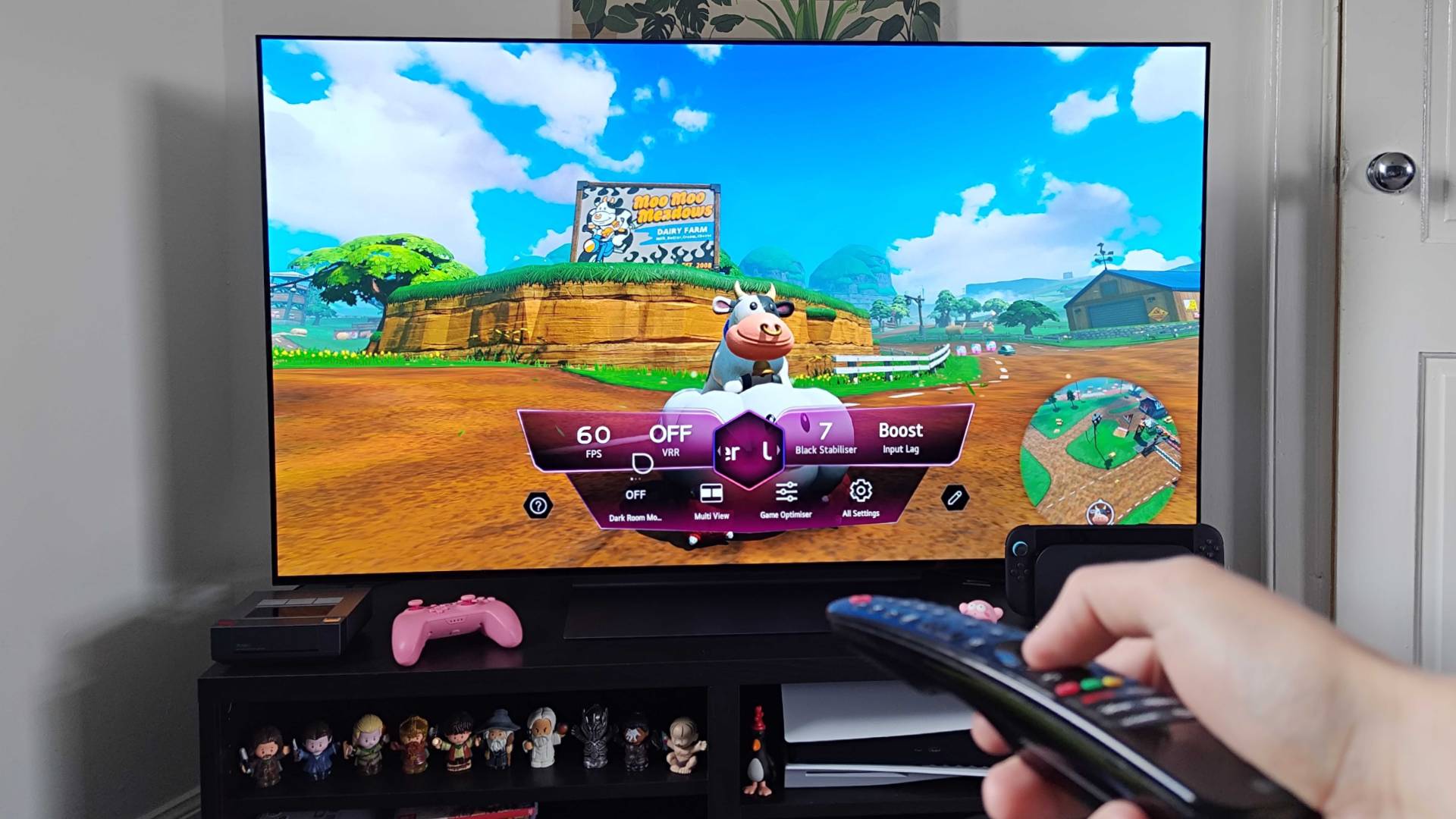 Hand holding remote in front of LG OLED C4 TV with Mario Kart World gameplay on screen featuring Moo Moo Meadows and Cow.
