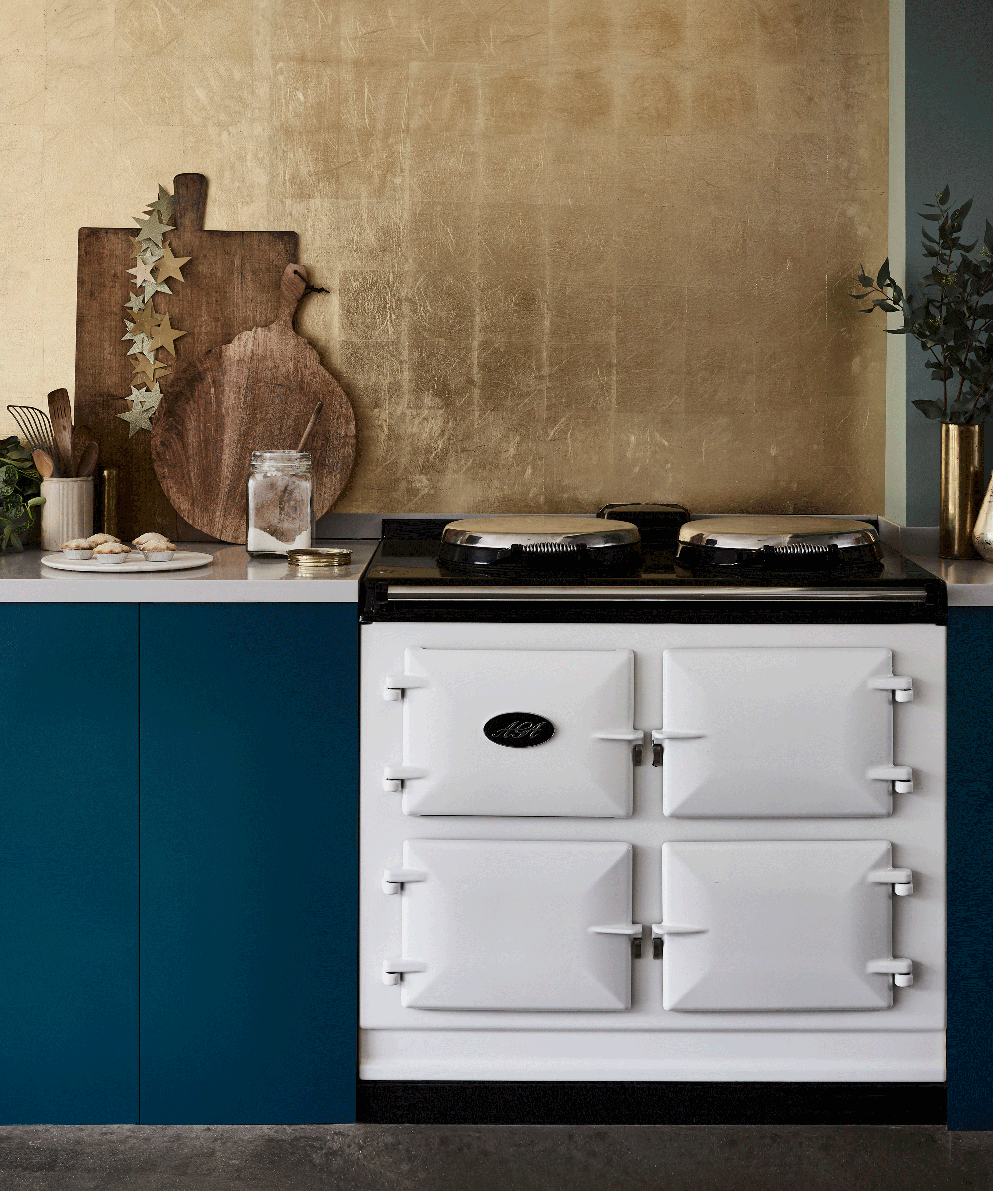 kitchen with white aga, blue cabinetry and a gold splashback
