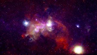 A vibrant purple, pink and yellow-ish image of the Milky Way's heart. It looks like blotches of glowing spots with speckles of stars and other galaxies in the background.