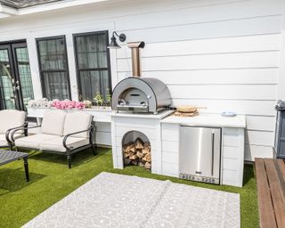 Cozy outdoor kitchen and living space design in light palette with wood-fired oven, and outdoor rug.