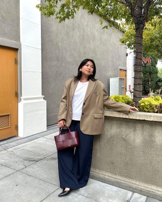 Marina wears a beige oversized blazer, navy trousers, white T-Shirt and burgundy handbag