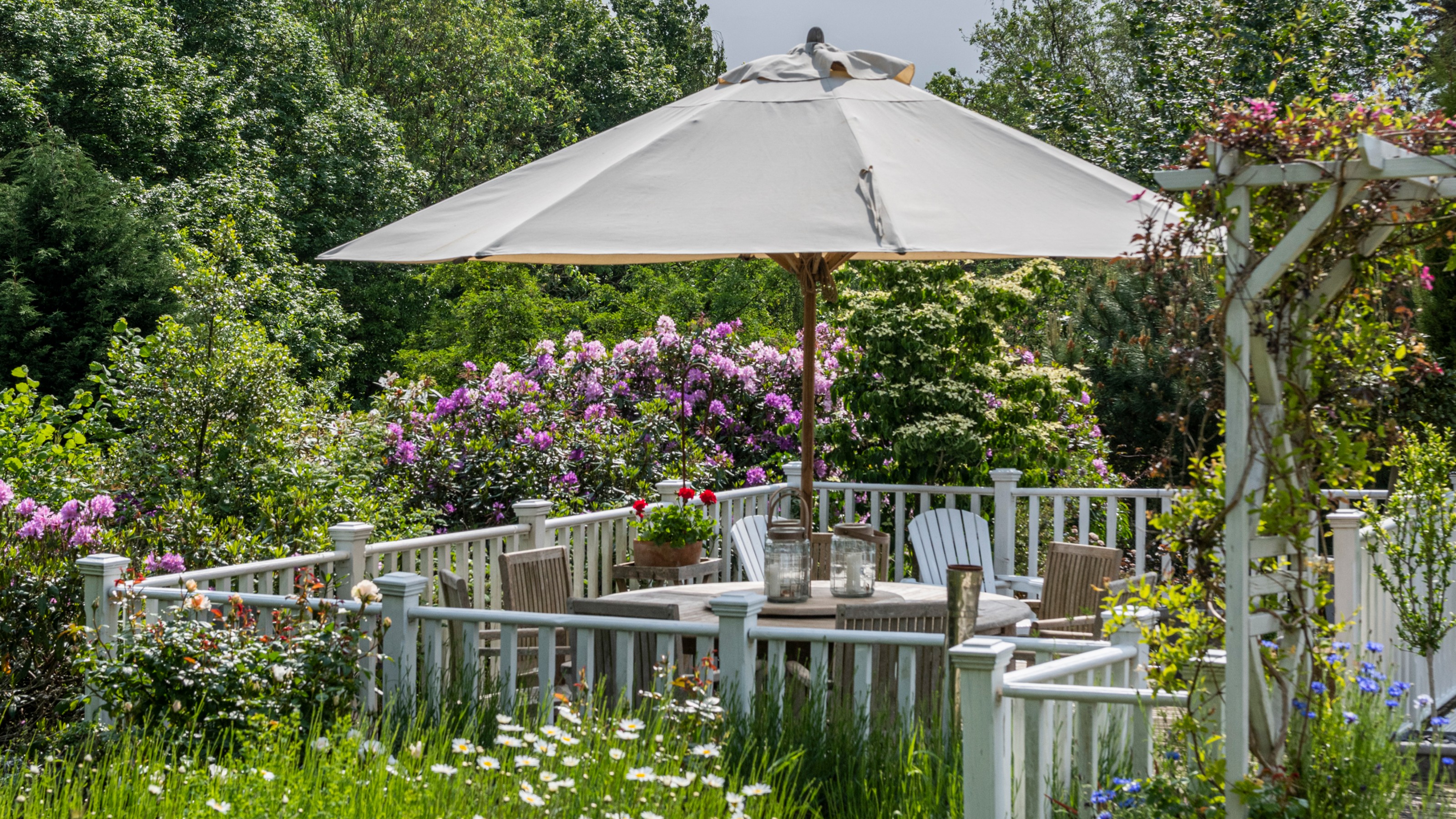 A blooming garden with an outdoor dining area and a white parasol