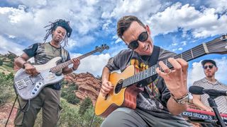 Closeup of Cory Wong with his acoustic guitar, his bassist on his right and his keyboardist on his left