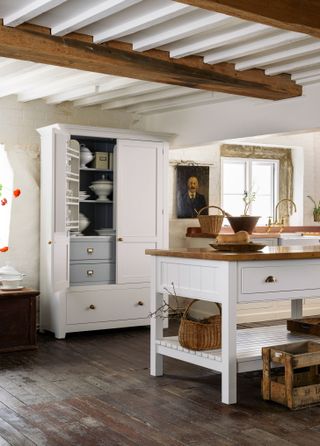 A traditional white kitchen with an island and wooden worktops and wooden ceiling beams