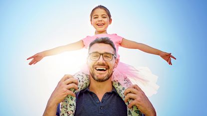 A smiling dad carries his daughter on his shoulders.