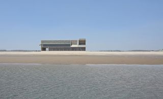 View from the sea and shoreline, looking at the library building in the distance on a sunny day, blue clear sky