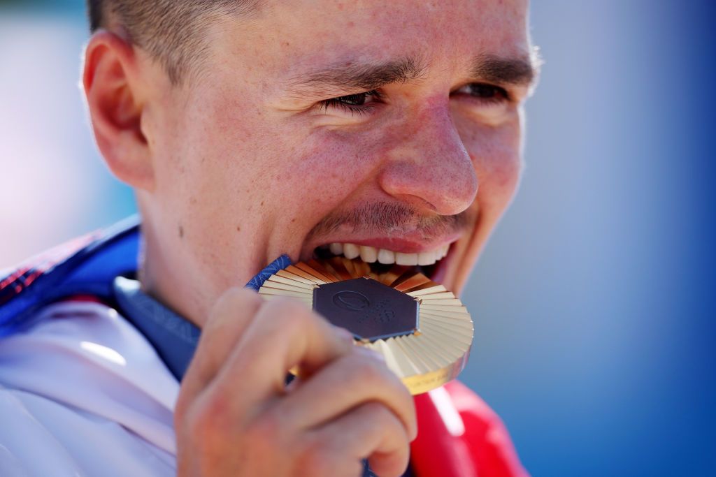 ELANCOURT FRANCE JULY 29 Gold medalist Thomas Pidcock of Team Great Britain bites his medal on the podium during the Mens CrossCountry on day three of the Olympic Games Paris 2024 at Elancourt Hill on July 29 2024 in Elancourt France Photo by Jared C TiltonGetty Images
