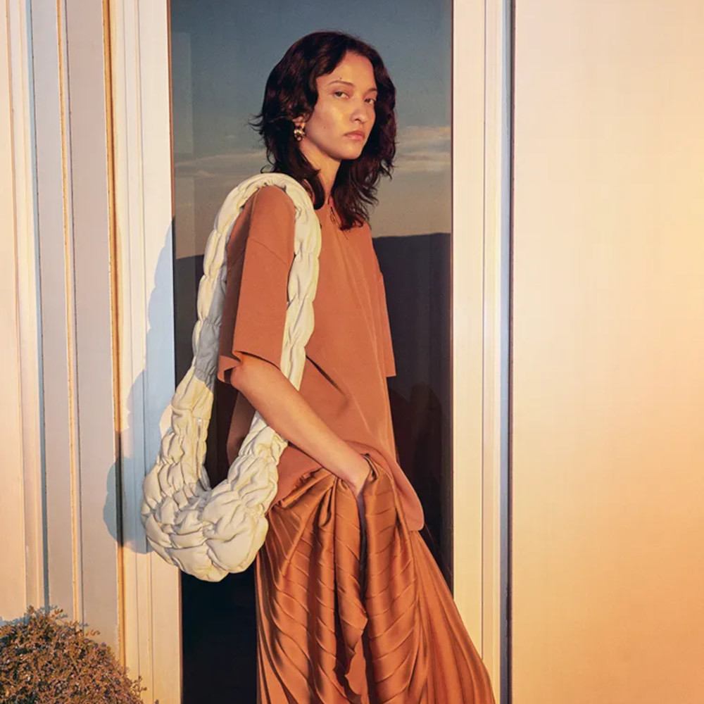 model wearing an orange dress with a beige bag 