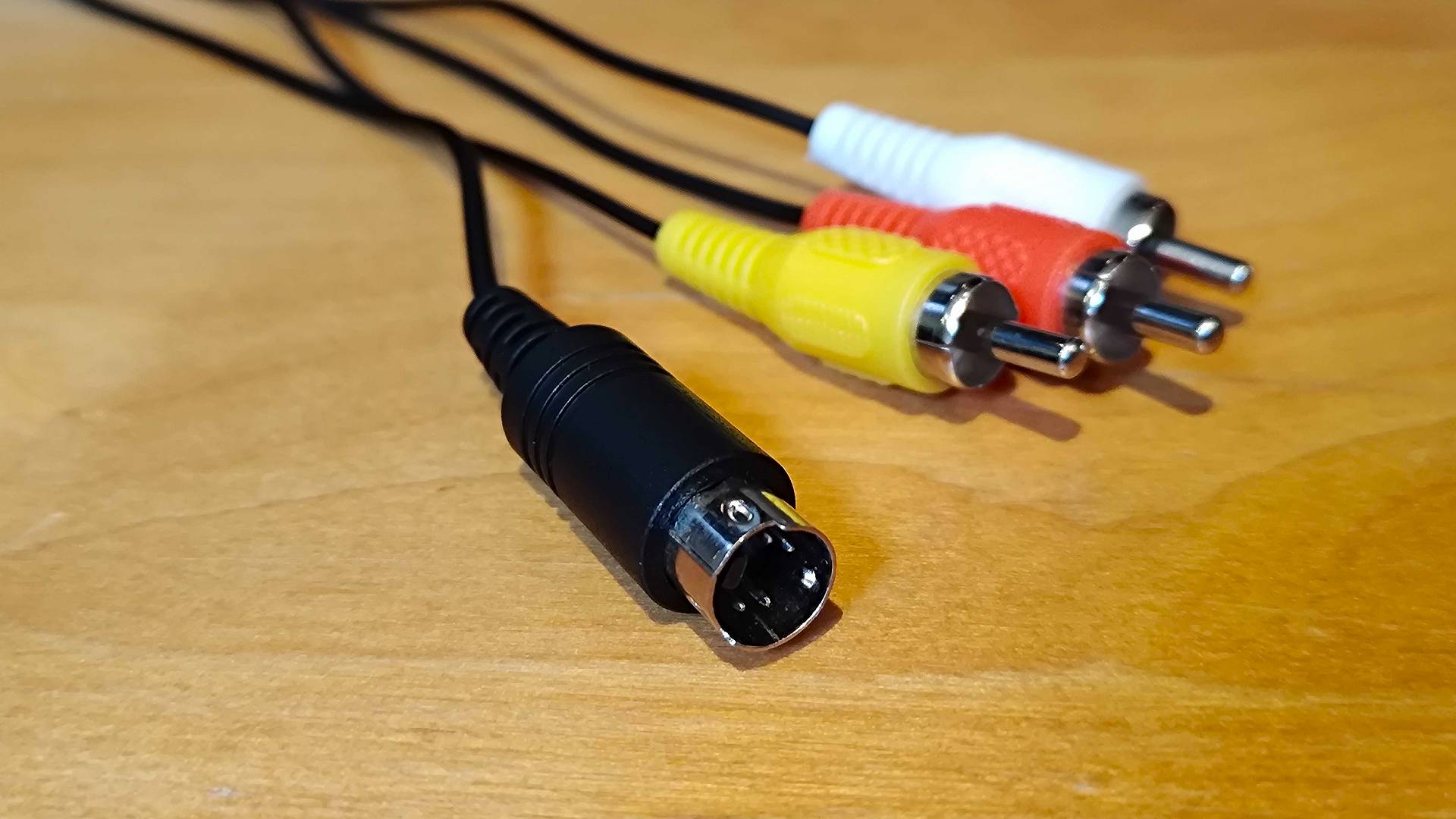 Black S-video cable next to yellow, red, and white RCA cables on woodgrain desk.
