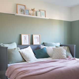 green bedroom with grey day bed white shelf pink throw framed art prints