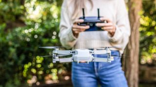 Cropped front view of unrecognizable young woman controlling and flying small drone in the city park