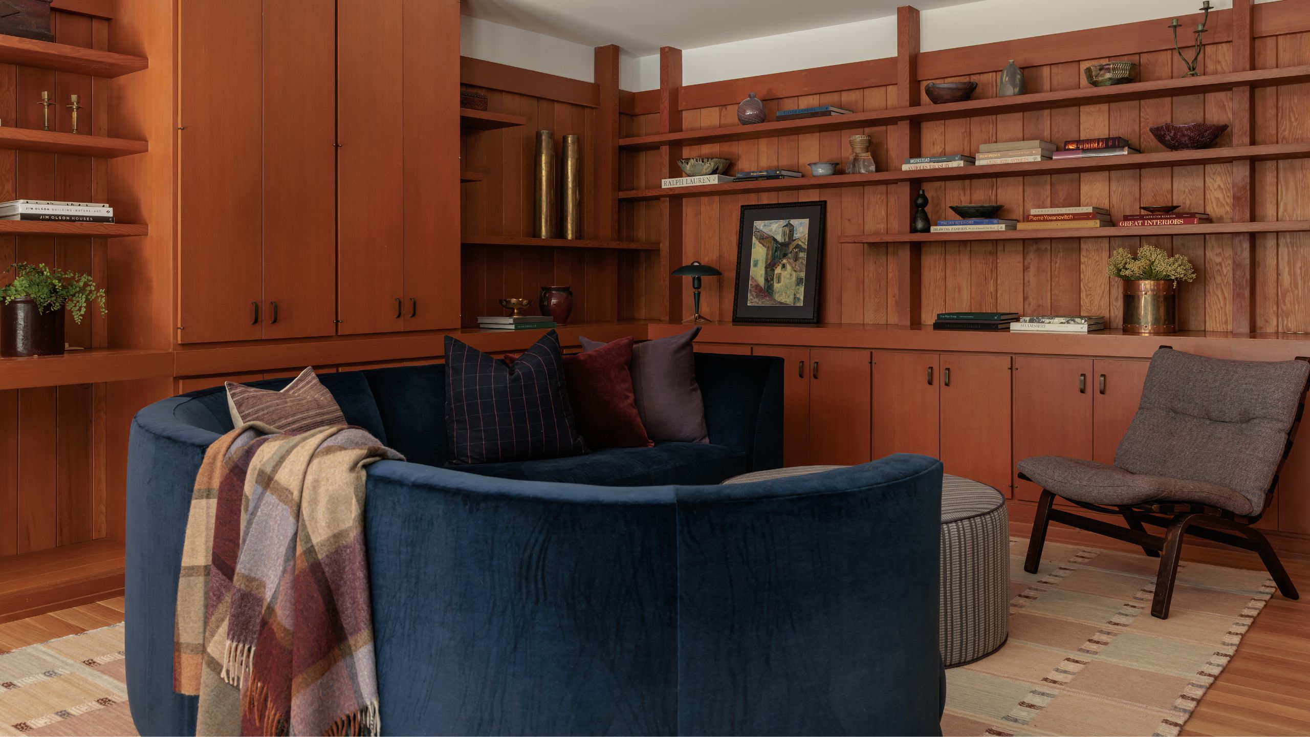 a wood clad family room surrounded with storage and open shelves with a curved navy sofa
