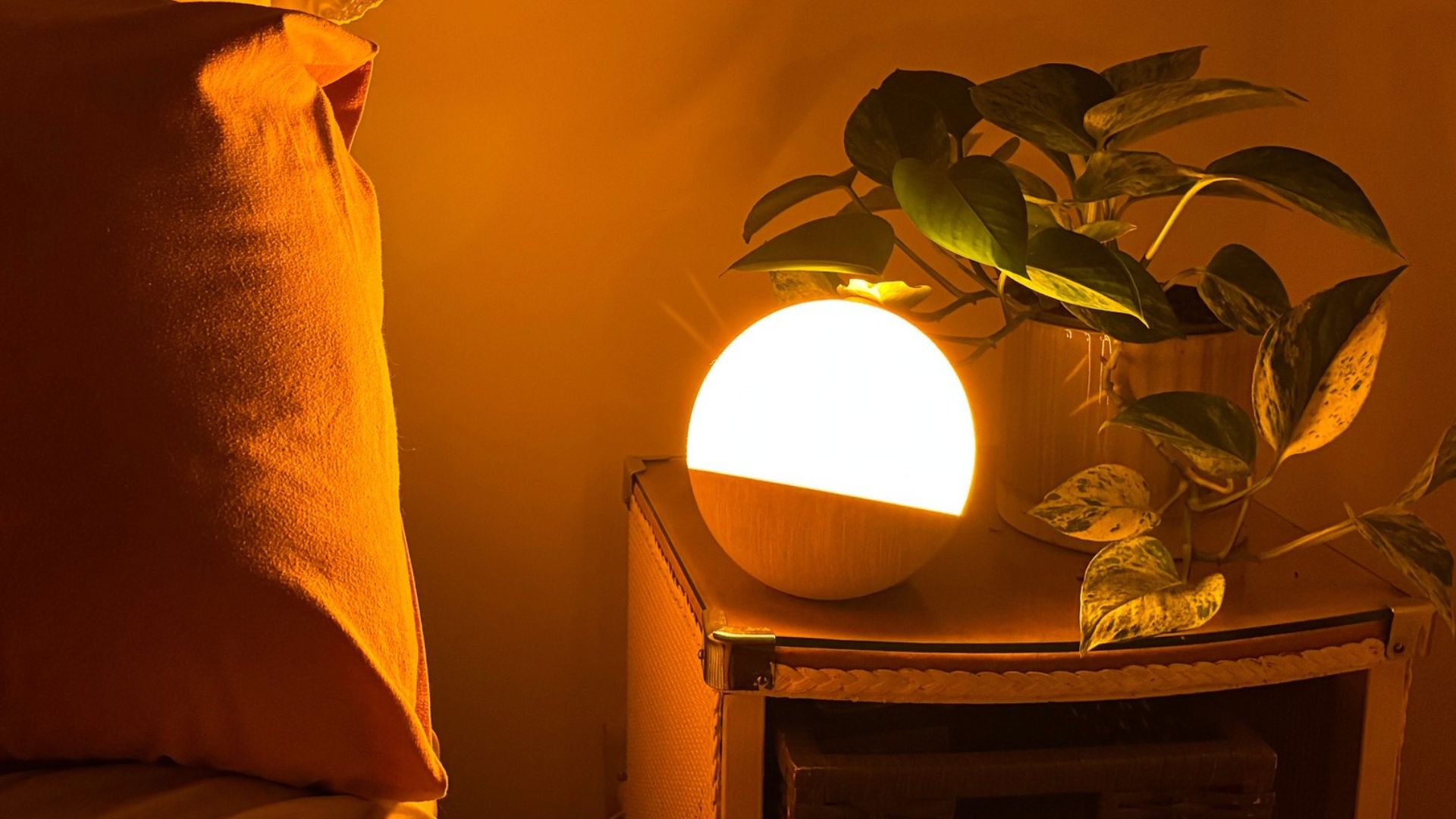 The image shows a circular sunrise alarm emitting a soft orange glow, placed clock on a nightstand