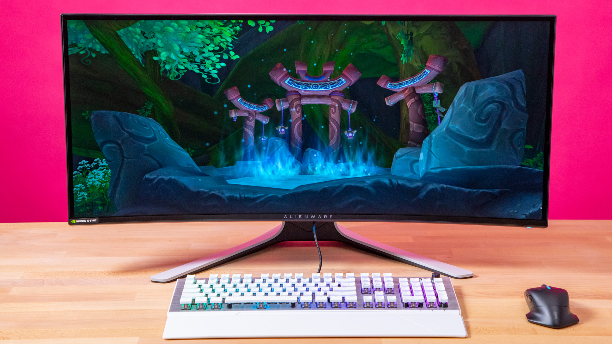 alienware monitor on a desk with a pink background a white keyboard