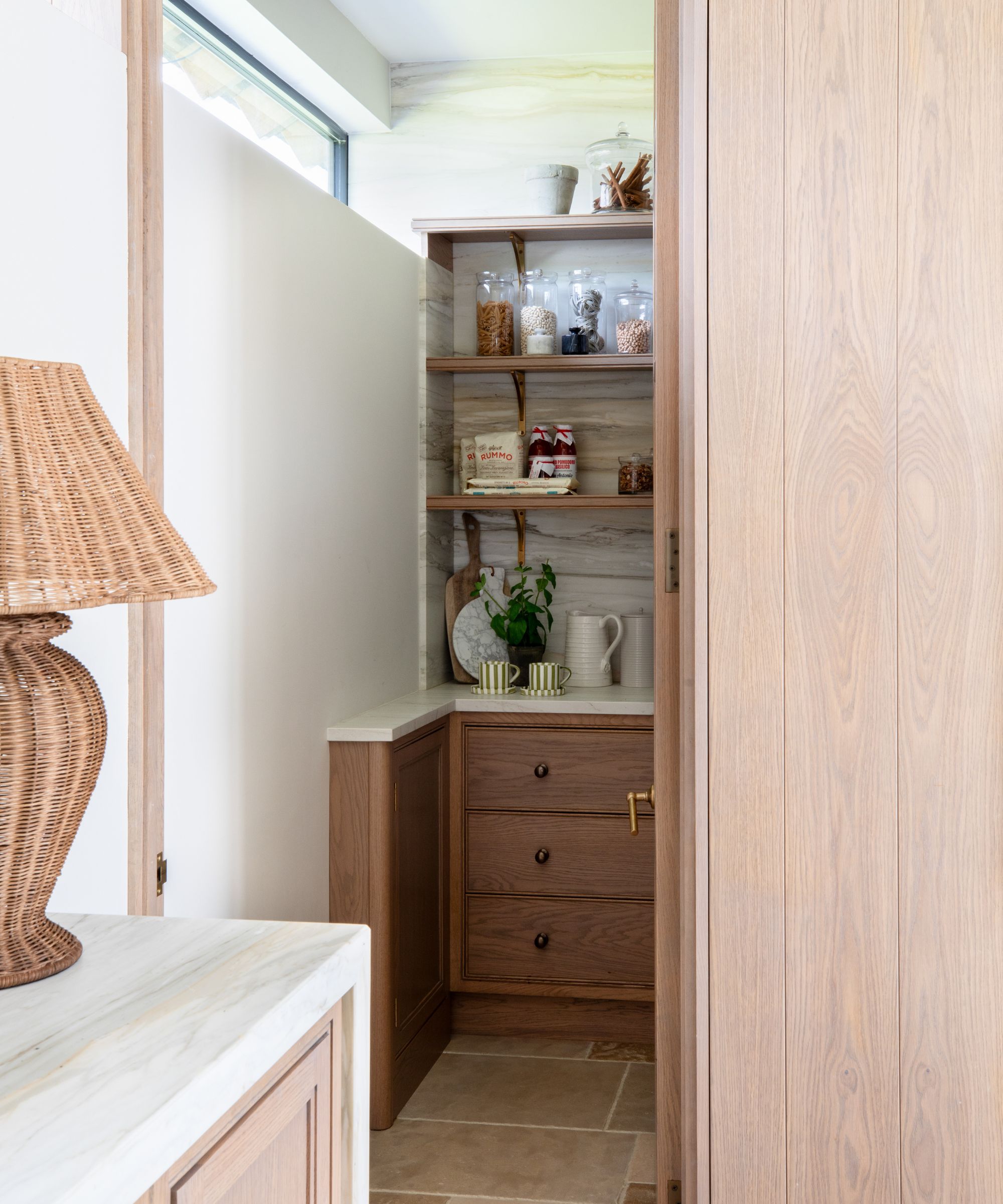 A view into a hidden pantry with wood cabinetry, wooden shelves, and marble countertops