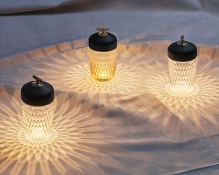Three portable lamps in textured crystal, casting patterned lights and shadows on the surface below