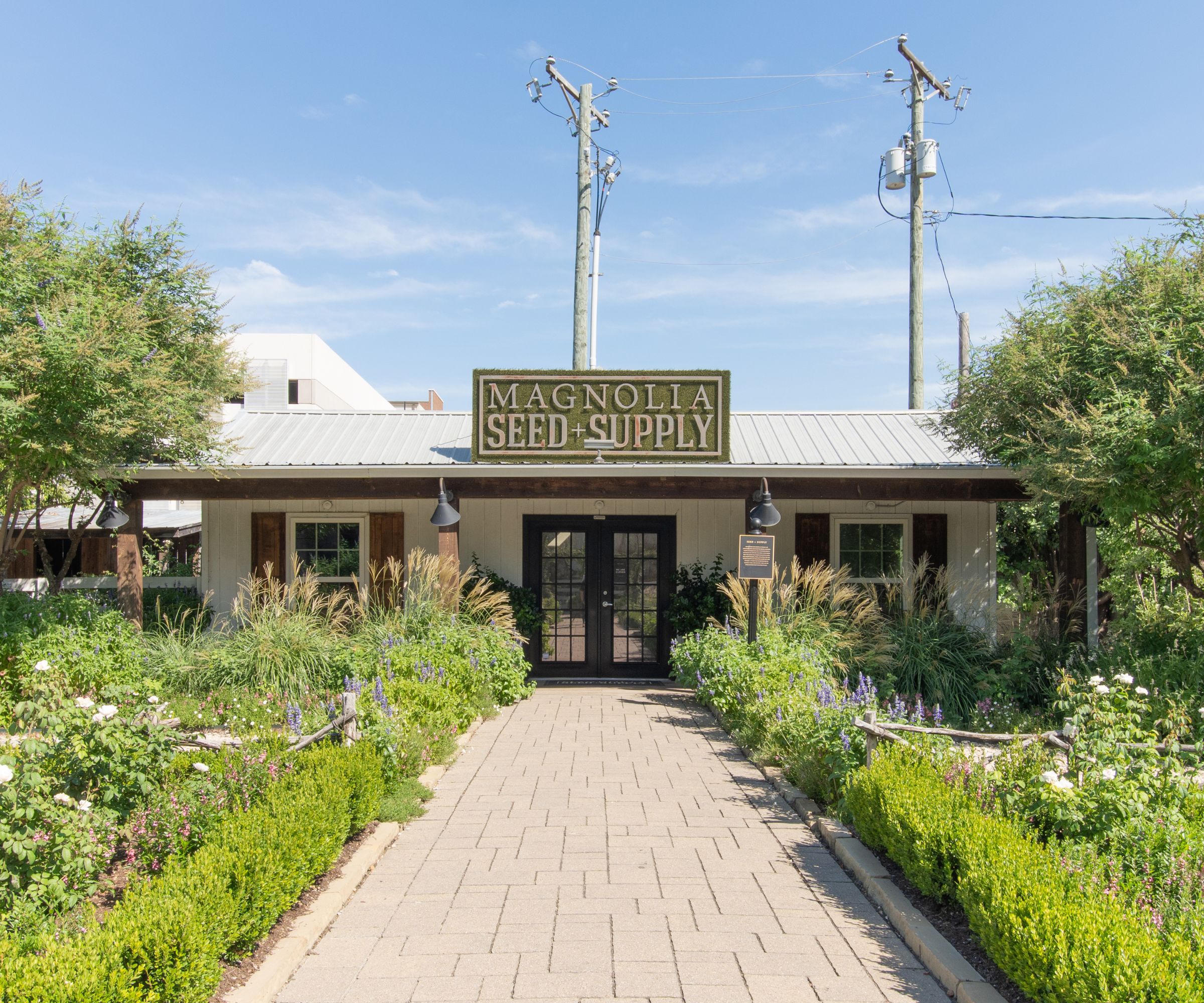 Seed and supply building with large door and brick path with greenery and flowers