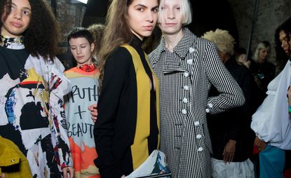 Model wears a black and white check coat, another wears a high neck jumper with yellow lapels