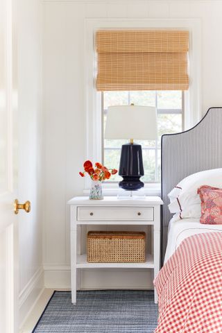 bedroom with bamboo blind white bedside table bedhead and red gingham cover and red cushion in room with white walls