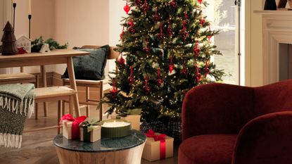 a christmas tree in a modern scandi room with a wood table and red velvet chair
