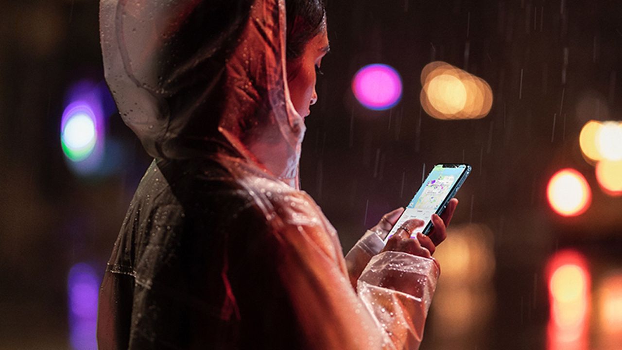 Apple iPhone XR being used by a woman in a rain coat in the rain, with water dripping down her hood