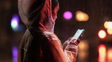 Apple iPhone XR being used by a woman in a rain coat in the rain, with water dripping down her hood