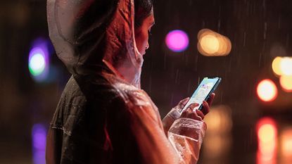 Apple iPhone XR being used by a woman in a rain coat in the rain, with water dripping down her hood