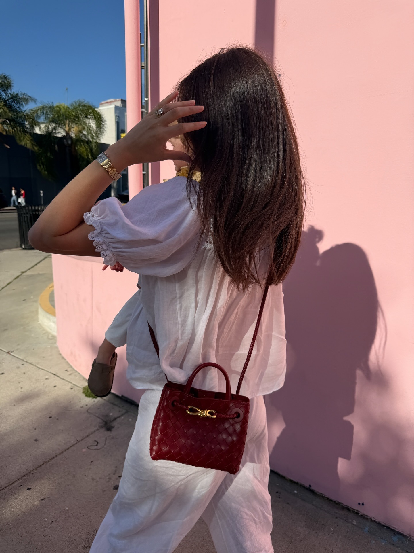 @ilanatorbiner wearing a pretty white boho blouse with white linen pants and a burgundy Bottega Veneta Andiamo bag.