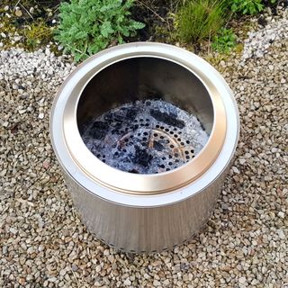 The stainless steel Solo Stove Ranger fire pit being cleaned in a gravel garden