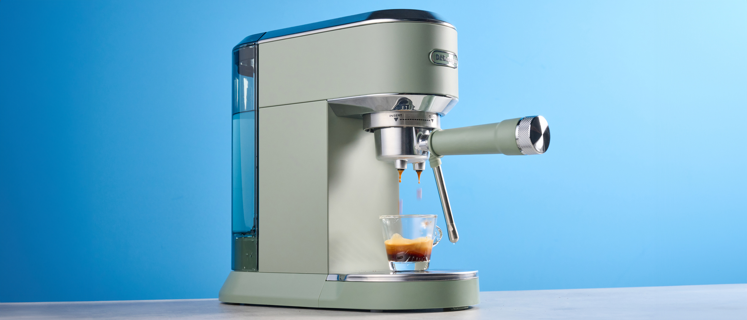 DeLonghi Dedica Duo in the green colorway with accessories photographed on a blue background. 